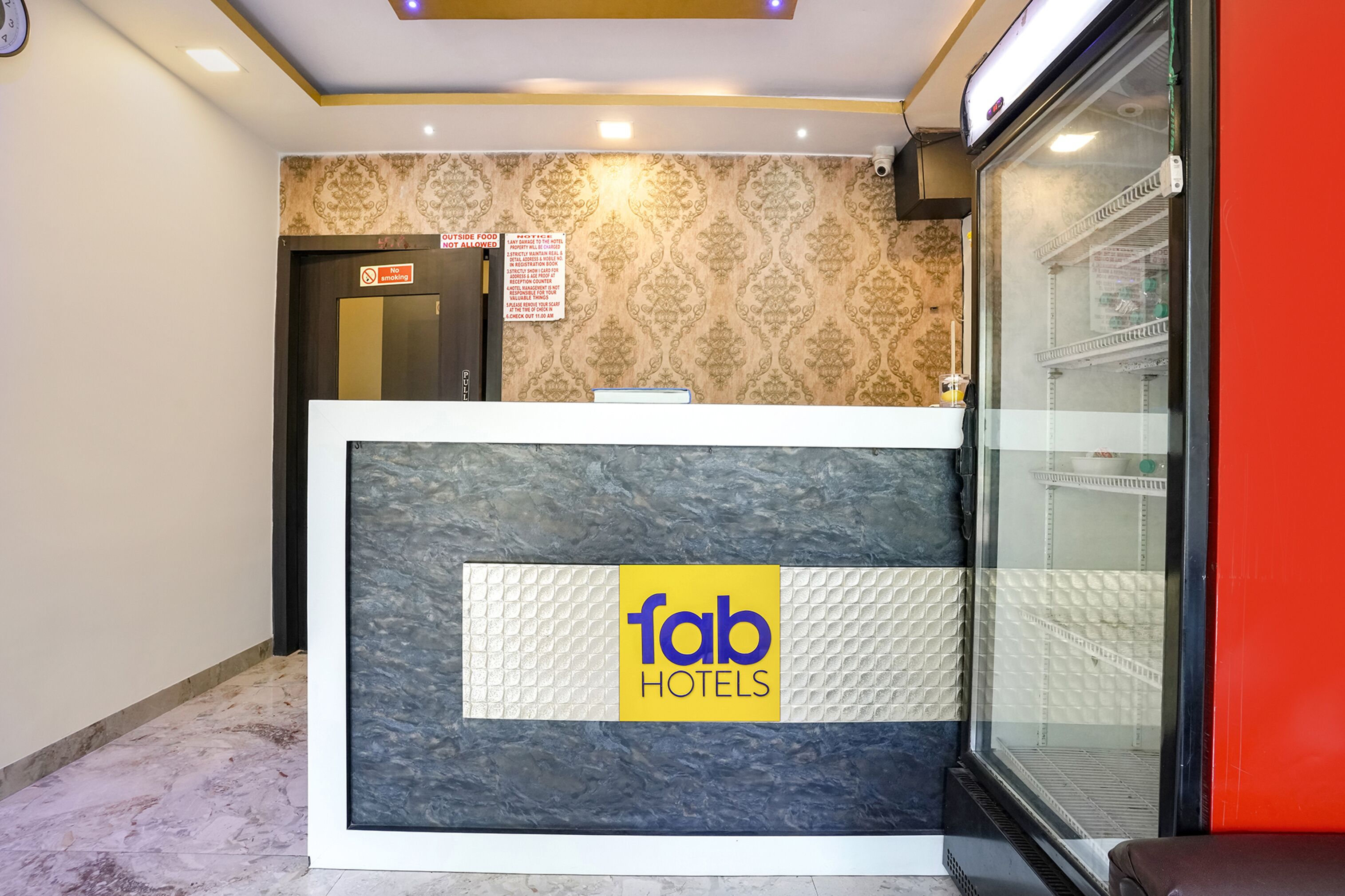 A hotel reception desk with a 'fab hotels' sign, a patterned wall, and a glass display case with shelves.