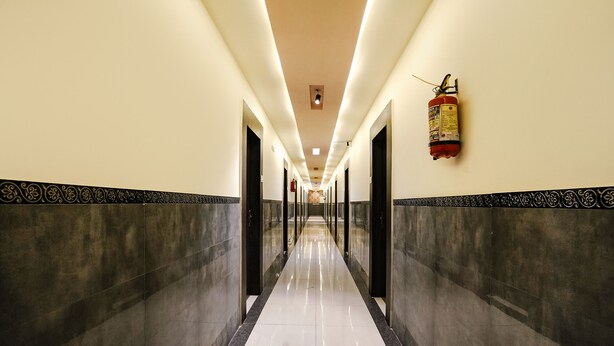 A long, well-lit hallway with a fire extinguisher on the wall and a ceiling light fixture. - Fabhotel Sai Vihar (Thane)