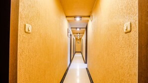 A long, narrow hallway with yellow walls and a black-tiled floor, leading to a door at the end. - Fabhotel Samrat (Nashik)