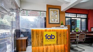 A reception desk with a wooden finish and a sign reading "fab hotels". There are chairs and a small table to the right. - Fabhotel Samrat (Nashik)