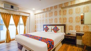 A hotel room with a large bed, a desk with a chair, and a window with curtains.