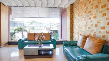 A modern lobby with a green sofa, a coffee table with a vase of flowers, and a patterned wall.