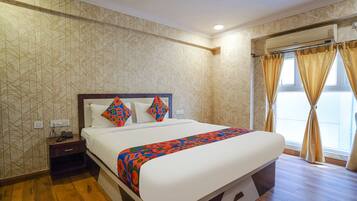 A hotel room with a large bed, a nightstand with a phone, patterned wallpaper, and a window with curtains.