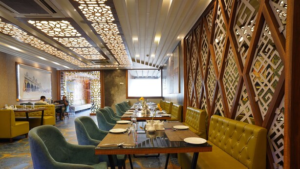 A restaurant with a long table set for dining, surrounded by green upholstered chairs and yellow cushioned booths. - Fabhotel Prime Signature Inn (Bengaluru)