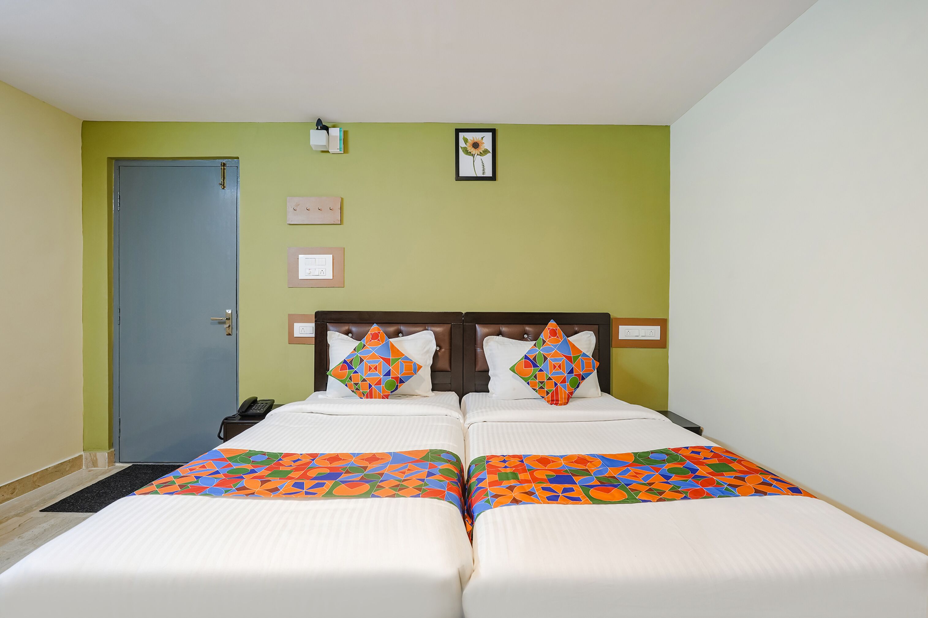 A hotel room with two beds, a blue door, and a wall-mounted light fixture.