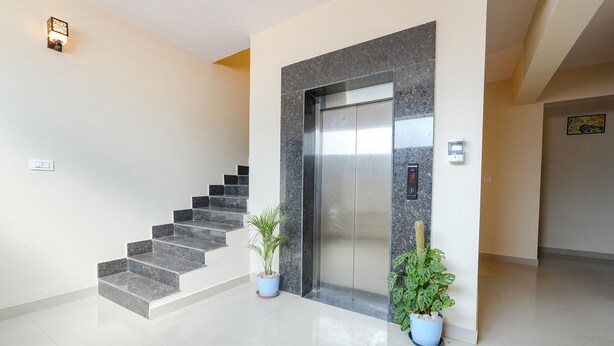 Um elevador moderno com detalhes em mármore, uma escadaria com degraus cinzentos e duas plantas em vasos.