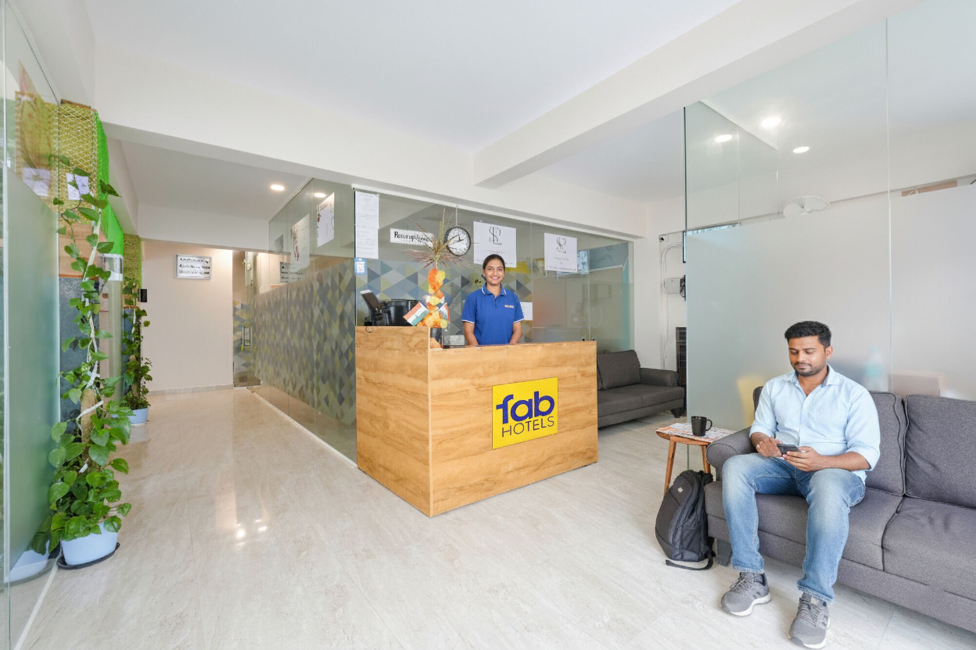 Zona de recepción con un mostrador de madera con la etiqueta 'fab hotels', una recepcionista, un sofá y una planta.