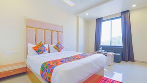 A hotel room with a large bed, a bedside table, a window with curtains, and a view of the outdoors.