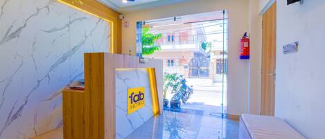 A hotel reception area with a marble wall, a wooden reception desk, and a ceiling fan.