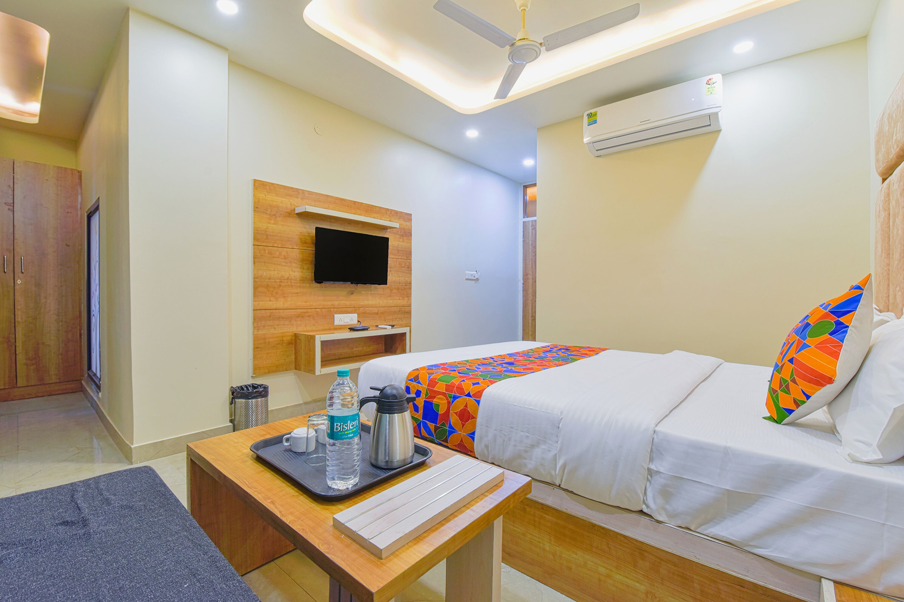 Une chambre d’hôtel avec deux lits, un bureau avec un clavier, une machine à café, une bouteille d’eau et un téléviseur fixé au mur.