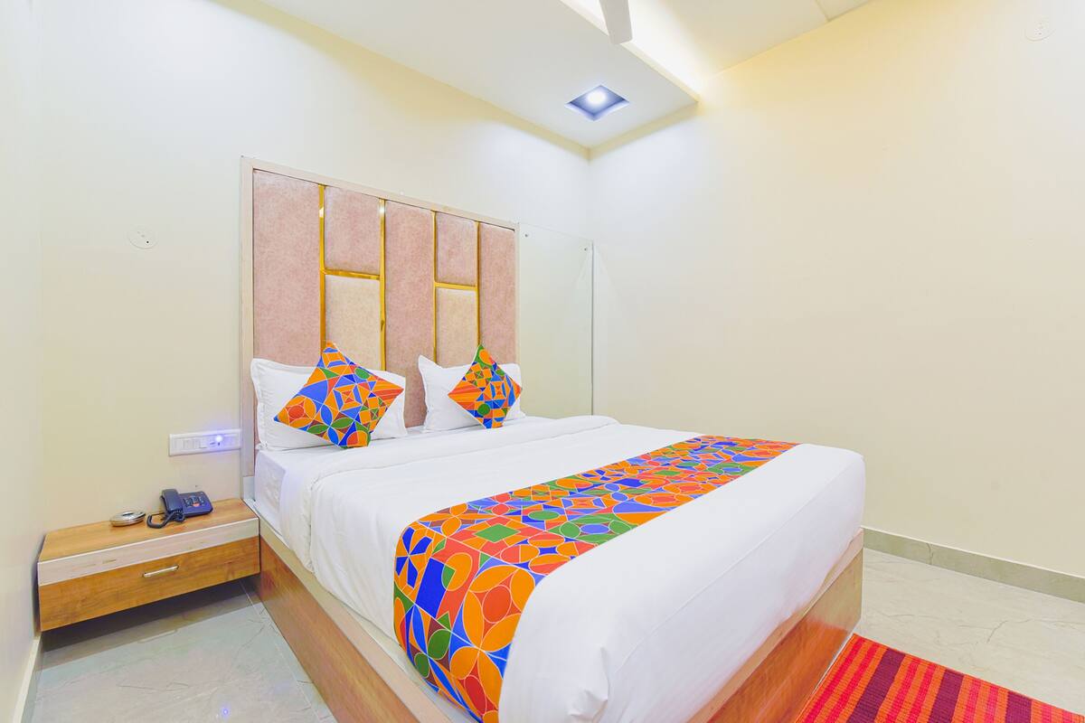 Een hotelkamer met een bed, nachtkastje, telefoon en plafondlamp.