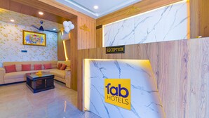 A reception area with a marble wall, a reception desk, a sofa with red cushions, and a ceiling fan.