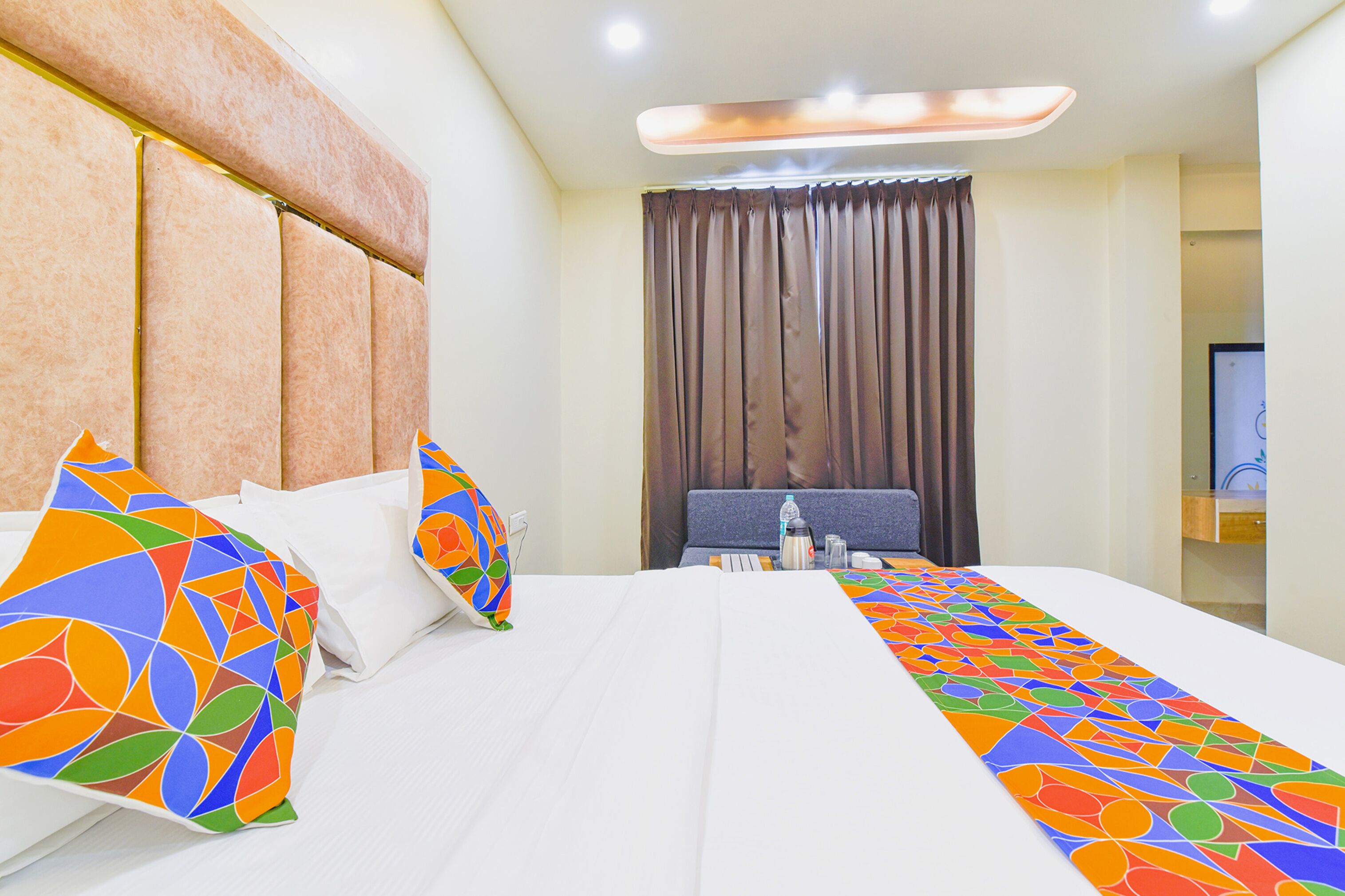A hotel room with a large bed, a headboard, a bedside table with a lamp, and a window with curtains.