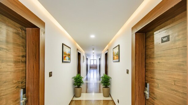 A modern hotel hallway with wooden paneling, numbered doors, and potted plants.
