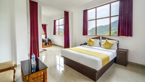 A hotel room with a large bed, a bedside table, a nightstand, a chair, and a view of the outdoors. - Fabhotel Abrigo Residency (Devikolam)