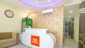 Un área de recepción con un mostrador blanco identificado como 'fab express', un reloj en la pared y una máquina expendedora verde.