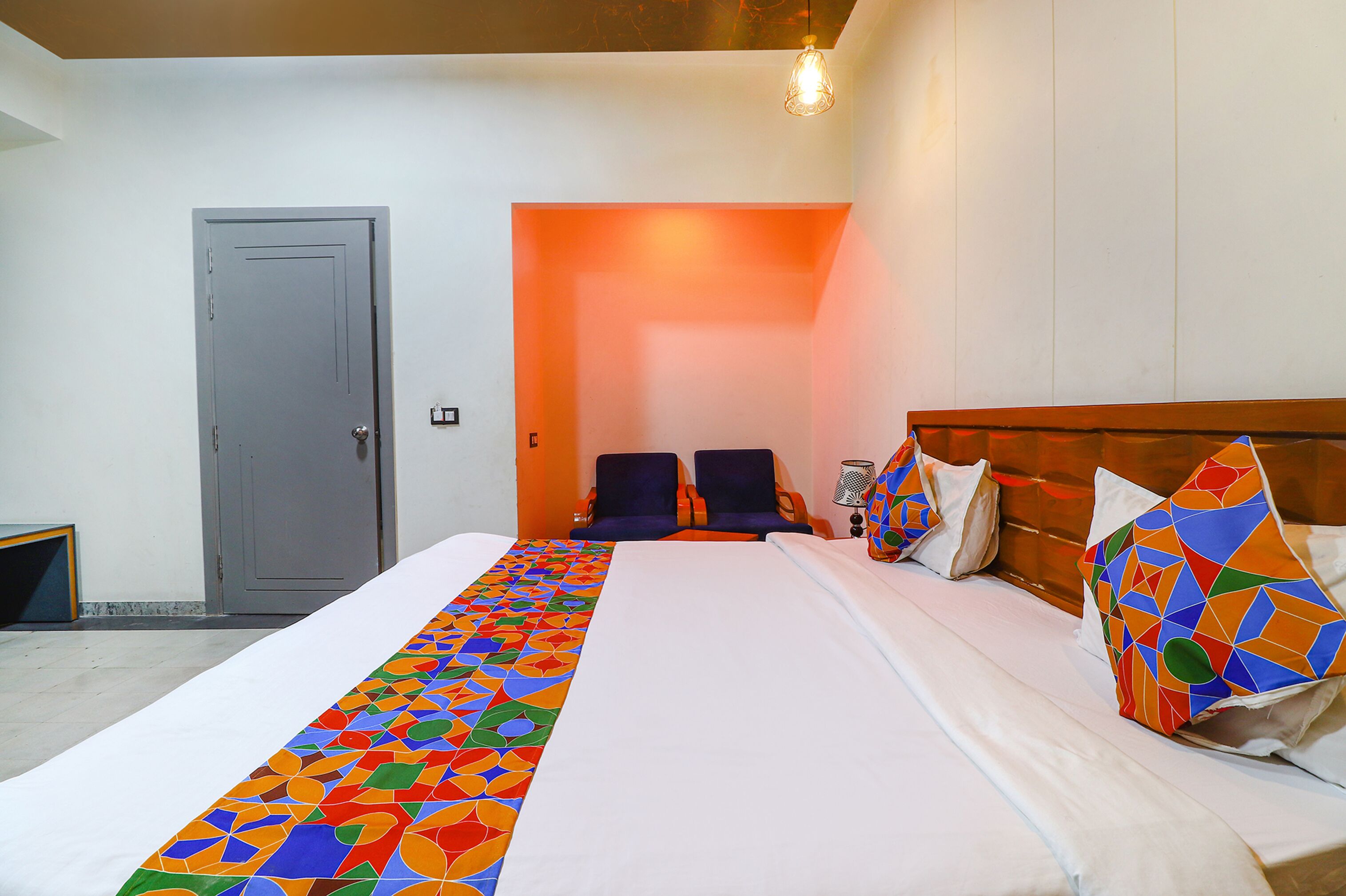 Een hotelkamer met een groot bed, een houten hoofdeinde en twee fauteuils.