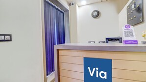A reception desk with a 'Via' sign, a clock, a QR code for contactless payments, and a window with curtains.
