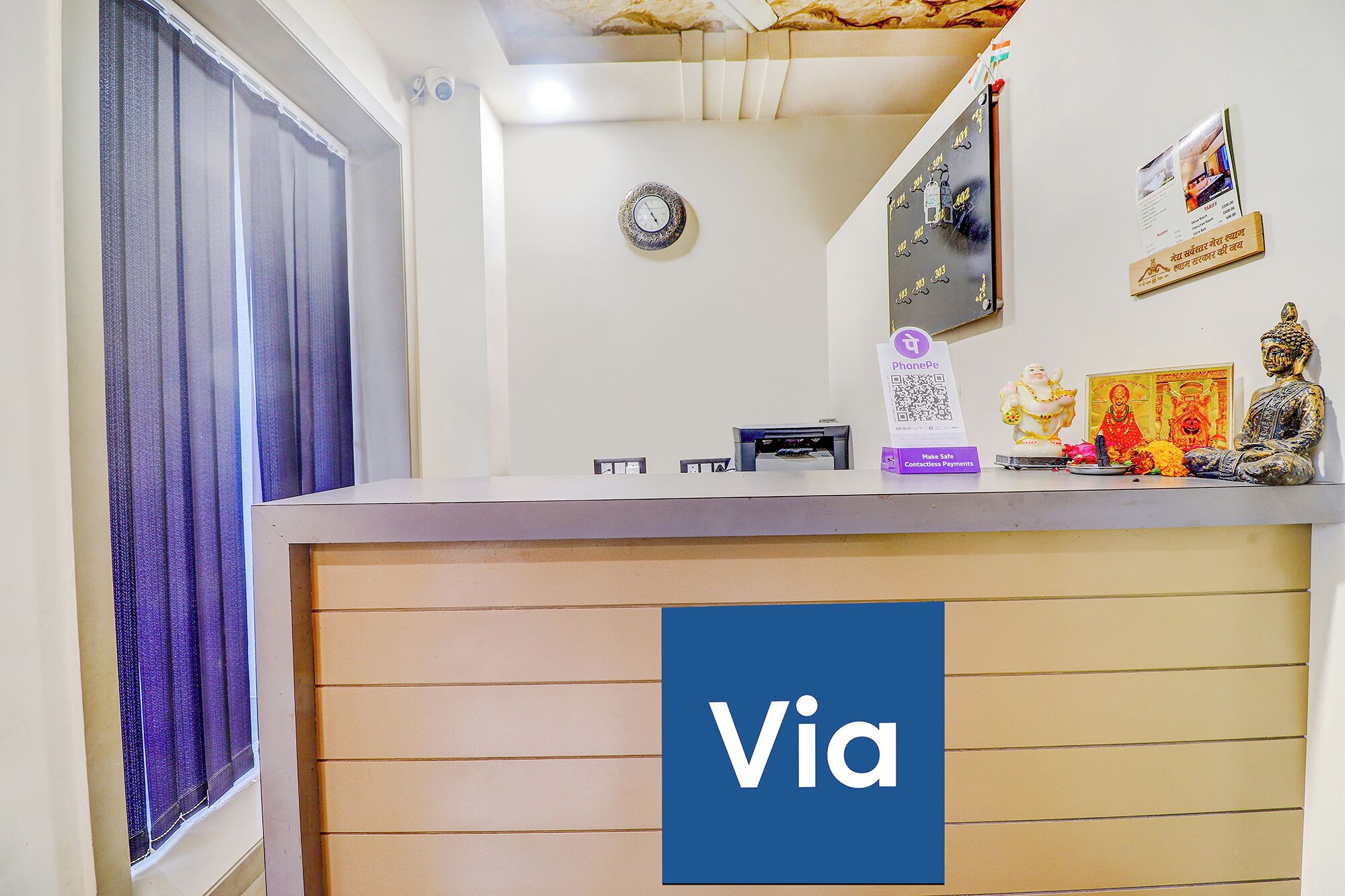 A reception desk with a 'Via' sign, a clock, a phone, and some religious statues.
