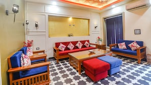 A living room with a sofa, armchairs, and a coffee table. There is a window with curtains, a ceiling fan, and an air conditioning unit.