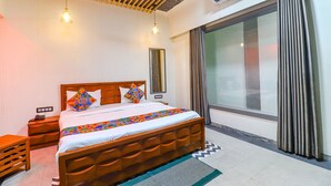 A bedroom with a wooden bed, a nightstand, a desk, and a large window with curtains.