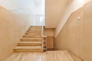 Una escalera con barandilla metálica que conduce a una plataforma, rodeada de paredes color crema y un suelo pulido.