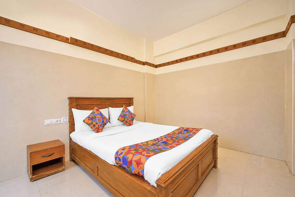 Uma cama bem arrumada com cabeceira de madeira, mesa de cabeceira e colcha estampada.