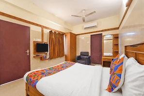 Ein Hotelzimmer mit einem Bett, einem Fernseher, einem Sessel, einem Schreibtisch mit Spiegel und einer Klimaanlage.