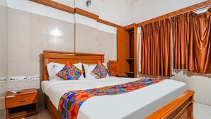 Habitación de hotel con una cama de madera, paredes blancas, piso de baldosas y un amplio ventanal con cortinas.
