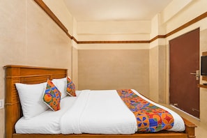 Una cama bien hecha con cabecera de madera, ropa de cama blanca y almohadas coloridas con motivos geométricos.