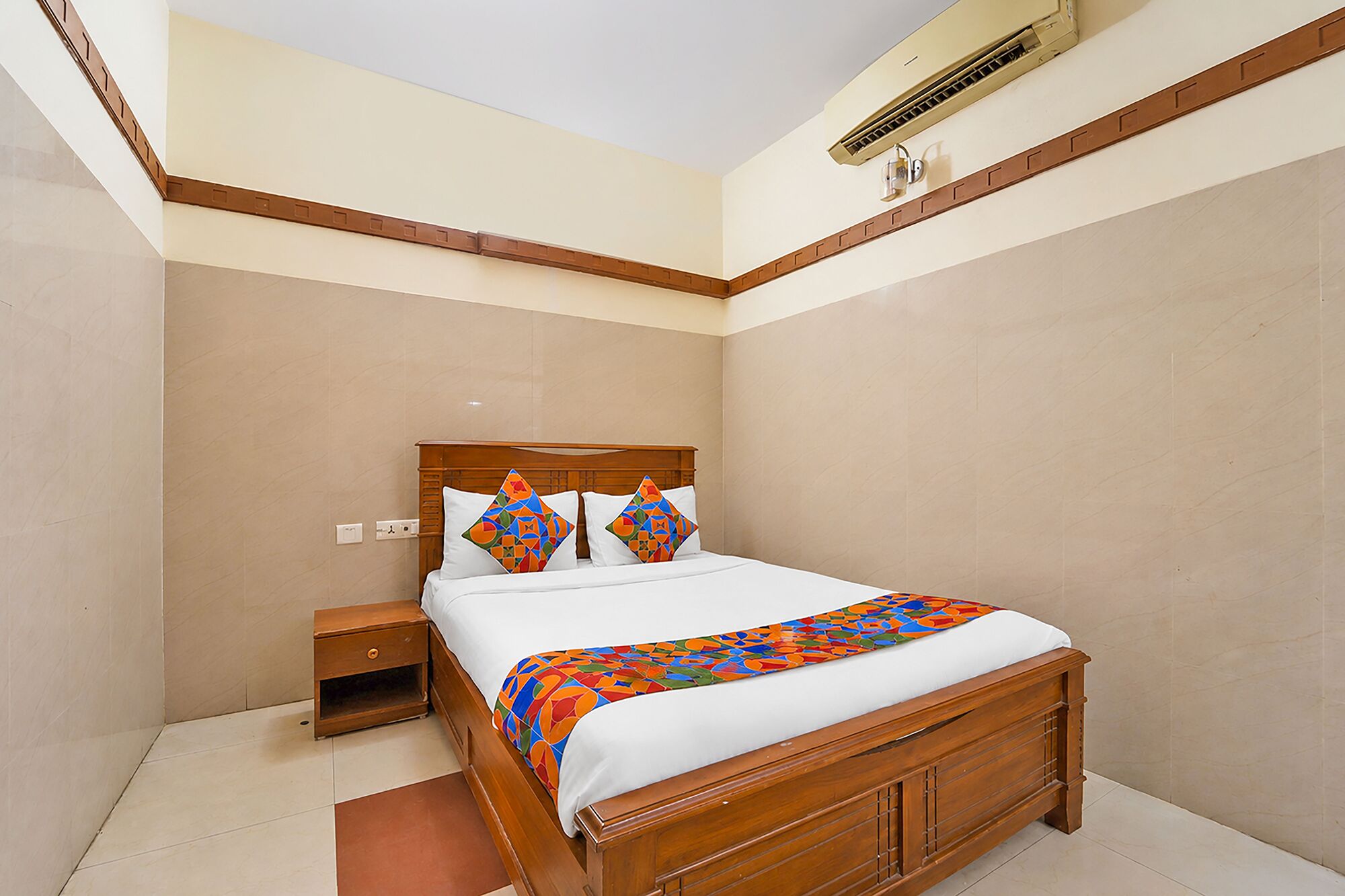 Ein Hotelzimmer mit einem hölzernen Bett, einem Nachttisch, einer wandmontierten Klimaanlage und einem Fliesenboden.