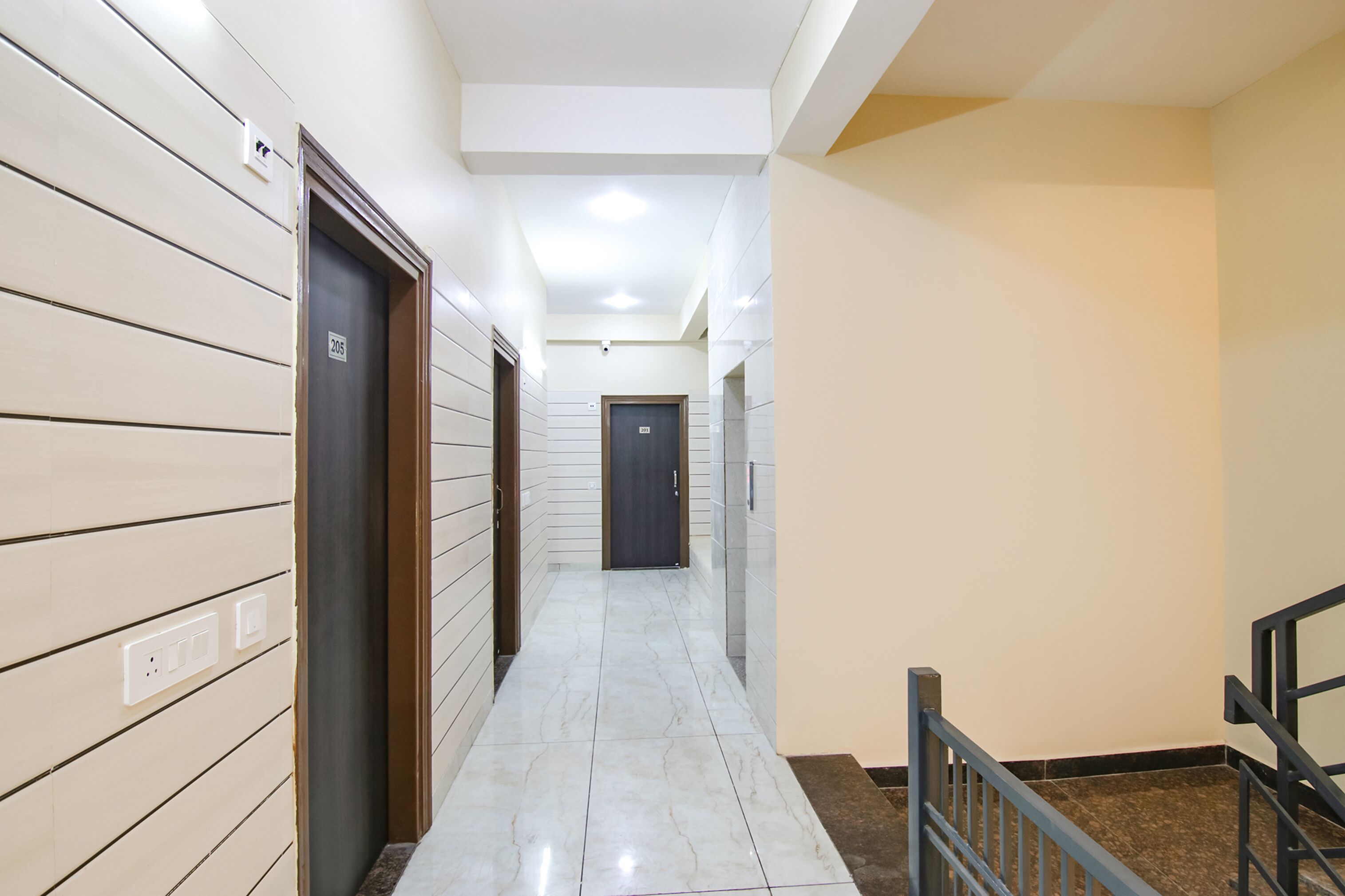 A corridor with a tiled floor, a door with a number, and a staircase with a metal railing.