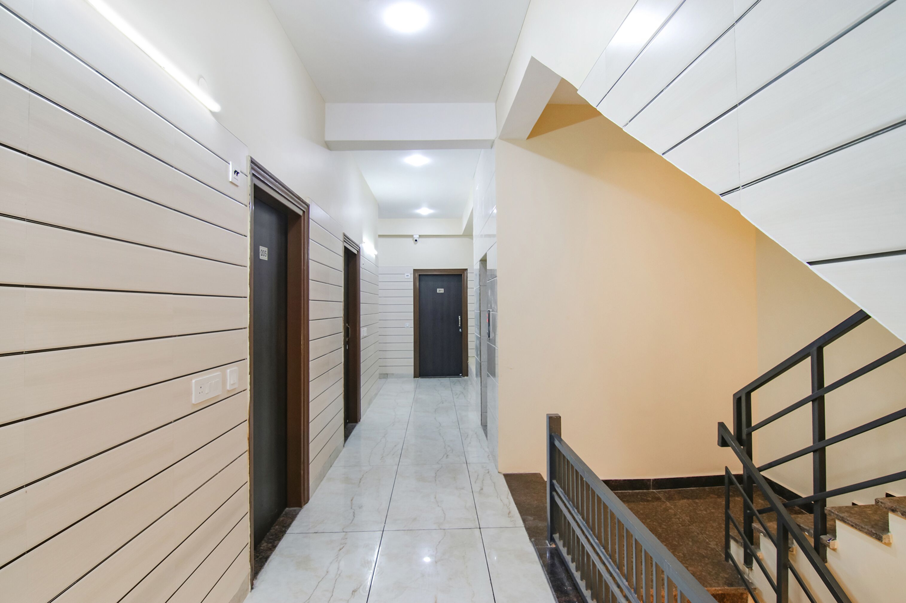 A narrow hallway with a marble floor, a staircase with a black railing, and doors on both sides.