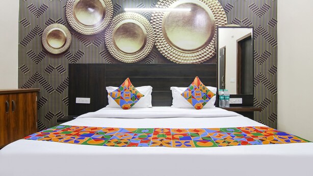 A hotel room with a large bed, two pillows with colorful geometric patterns, a mirror, and a patterned wall. - Fabhotel Gg Residency (Mohali)