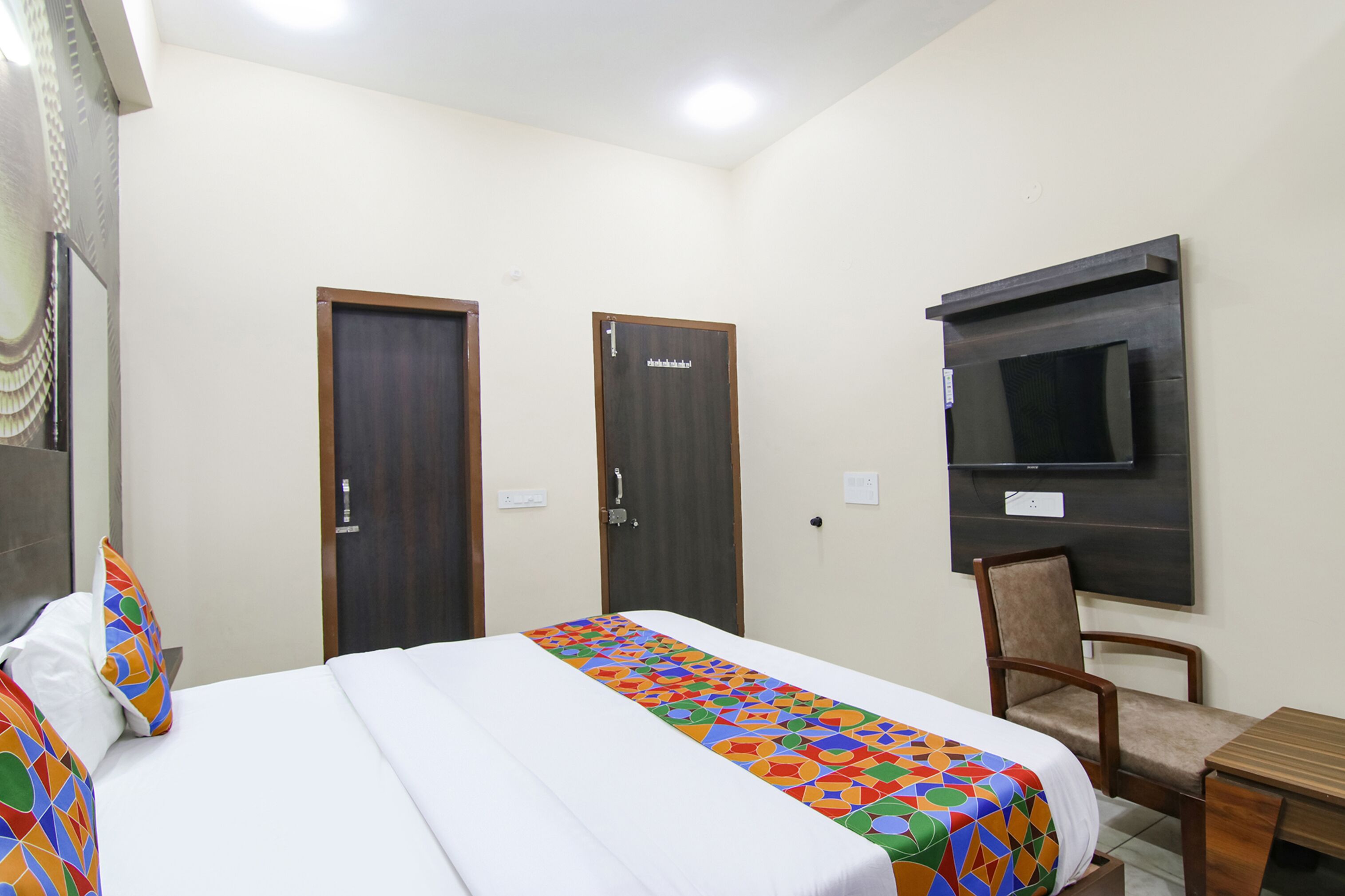 A hotel room with a bed, a chair, a small table, and a TV mounted on the wall.