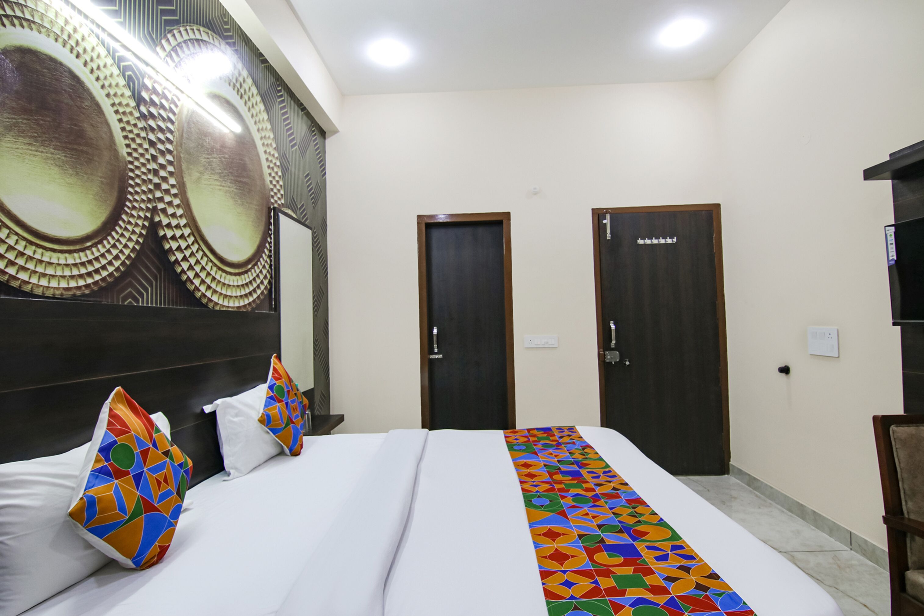 A hotel room with a large bed, two doors, and a decorative wall panel.