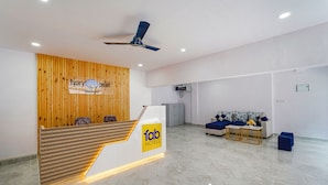 A hotel reception area with a wooden reception desk, a ceiling fan, a sofa, and a coffee table. - FabHotel Ivory Pearl Koramangala Bangalore (Bengaluru)