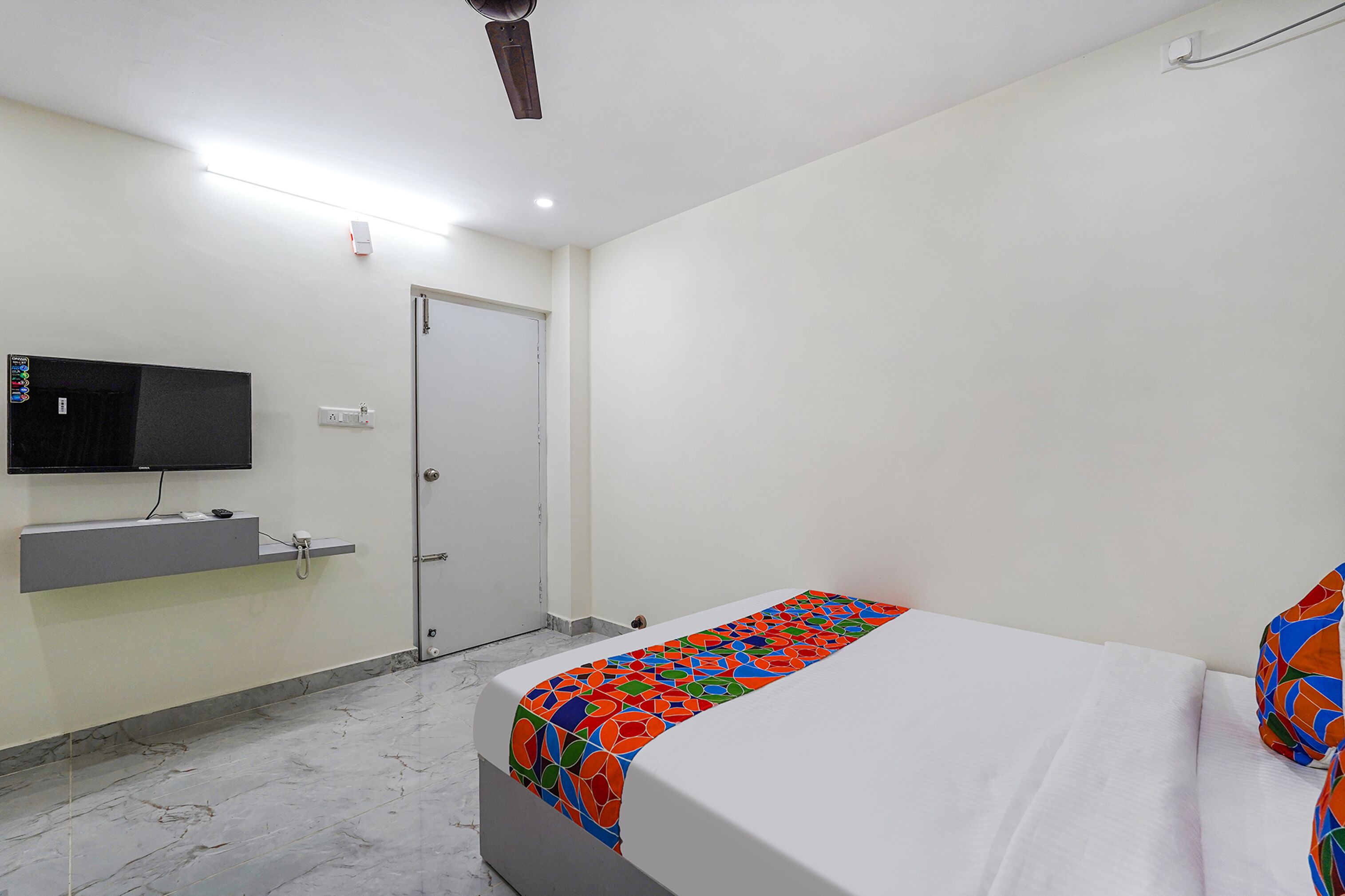 A hotel room with a bed, a television mounted on the wall, and a door.