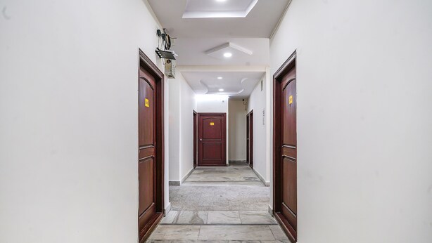 A hallway with marble flooring, wooden doors, and recessed lighting. - Fabexpress Venkateswara Atidhi (Hyderabad)