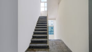 A narrow stairway with a handrail, leading to a landing with a window. - Fabexpress Venkateswara Atidhi (Hyderabad)