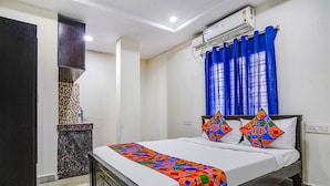 A neatly made bed with a colorful bedspread, a dark wooden headboard, and a blue curtain. - Fabexpress Venkateswara Atidhi (Hyderabad)