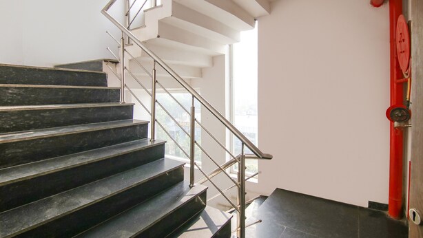 A staircase with black steps and a metal railing, leading to a landing with a red pipe and a lock. - Fabhotel Ssensse (New Delhi)