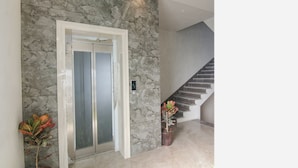 A modern elevator with a stone wall backdrop, a staircase, and potted plants. - Fabhotel Prime Royal Court (Ludhiana)