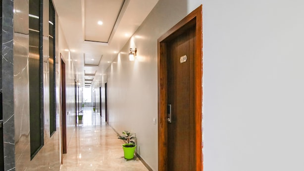A hallway with marble flooring, wooden doors, and potted plants. - Fabhotel Prime Royal Court (Ludhiana)