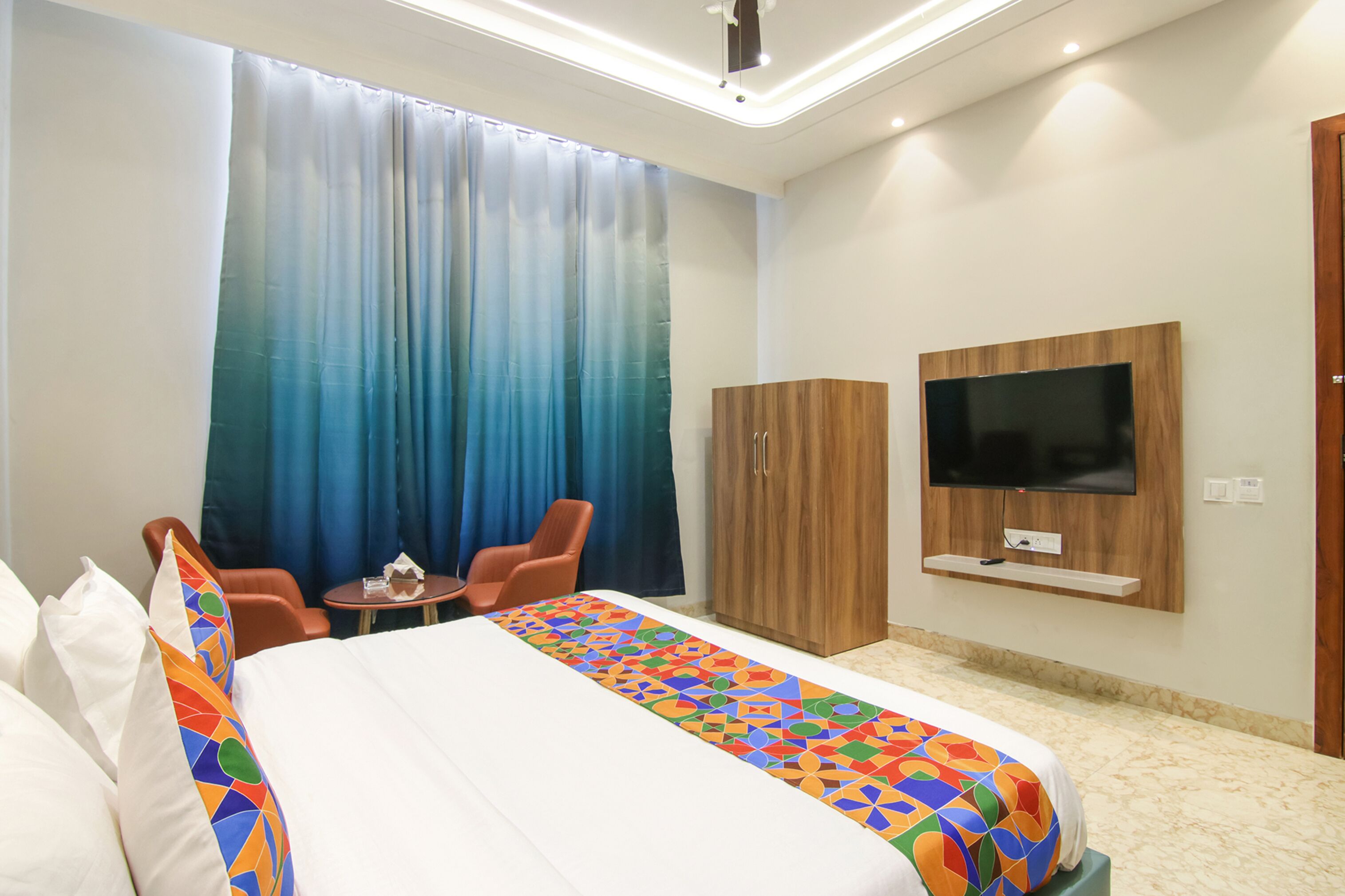 Ein Hotelzimmer mit Bett, Wandfernseher, Holzschrank und kleinem Tisch mit Stühlen.