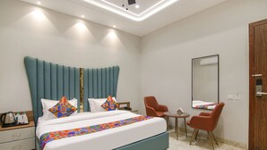 A modern hotel room with a large bed, a small table, two chairs, a wooden wardrobe, and a mirror on the wall. - Fabhotel Prime Royal Court (Ludhiana)