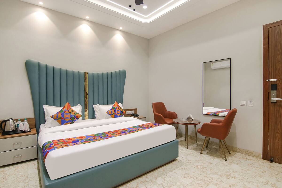 A modern hotel room with a large bed, a small table, two chairs, a wooden wardrobe, and a mirror on the wall.