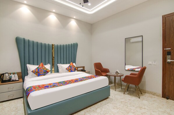 A modern hotel room with a large bed, a small table, two chairs, a wooden wardrobe, and a mirror on the wall.