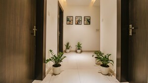 A hallway with wooden doors, potted plants, and three framed artworks on the wall. - Fabhotel Royal Palace Ii (Bhopal)