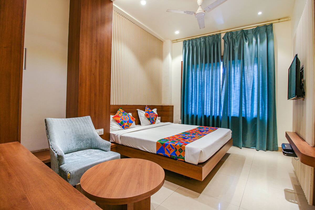 Une chambre d’hôtel avec un lit, une chaise, une petite table, un ventilateur de plafond et un téléviseur.
